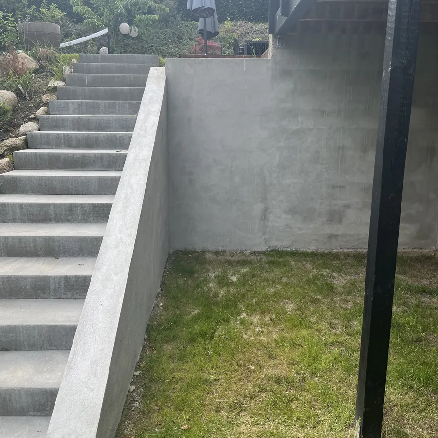 Betonmuren og trappen set fra plænen, før beklædning